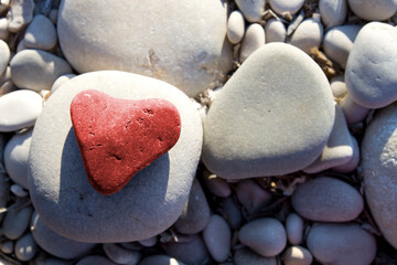 Obraz premium Red stone heart among river or sea pebble stones, Valentine's Day, perfect love