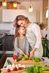 jolly child girl preparing a salad with her mother in the modern light kitchen, enjoy the process of preparing meal