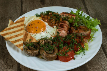 English homemade breakfast. Fried eggs with sausage, fried bacon, mushrooms, tomatoes, beans and toast