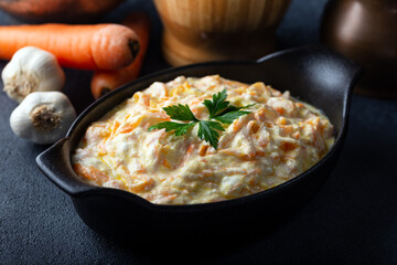 Carrot tarator in ceramic bowl with vegetable on dark background. Fresh carrot salad with garlic yogurt in bowl.