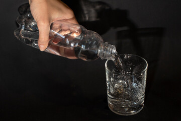 Hand pours water from a bottle into a glass glass on a black background