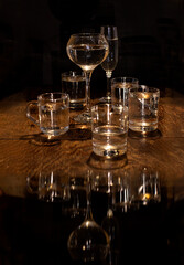 Dishes, on a wooden table, different glass goblets with drinks and their reflection