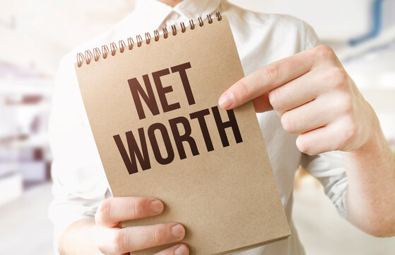 Text NET WORTH On Brown Paper Notepad In Businessman Hands In Office. Business Concept