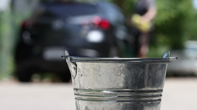 A man washes a car on the street, then throws a sponge into a distant bucket with splash of detergent, slow motion. A domestic hand washing car with soapy water.