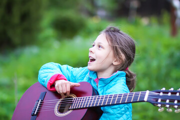 Little girl playing guitar and singing outdoors on green meadow at spring