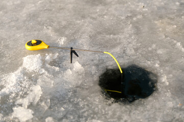 Naklejka premium A fisherman is fishing on a rod in an ice-hole on a winter fishing lake.