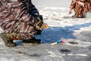 A fisherman is fishing on a rod in an ice-hole on a winter fishing lake.