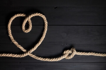Heart and rope knot on a black wooden background. Flat lay