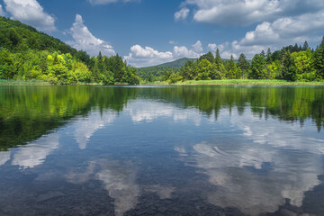 Clouds reflected in clean lake surrounded by hills and green lush forest, Plitvice Lakes National Park UNESCO World Heritage in Croatia