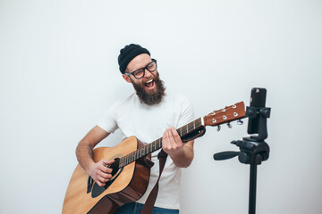 A young stylish guy with a beard wearing casual or music teacher playing guitar in front of...