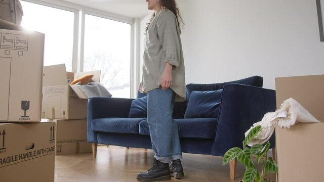 Young mixed ethnicity couple celebrating moving day in new home sitting on sofa in lounge surrounded by removal boxes together - shot in slow motion