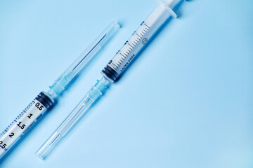 Two medical plastic disposable vaccination syringes with the needle in the cover cap isolated on the bright blue fond background