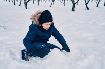Fototapeta na wymiar Caucasian boy warm and wearing a hat plays with the snow.