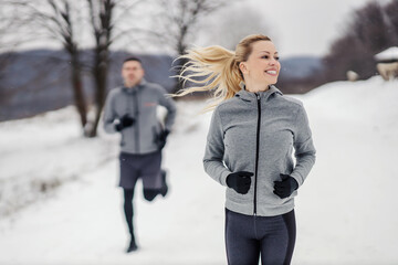 Happy fit sportswoman racing her friend in nature at snowy winter day. Fitness together, outdoor fitness, winter fitness
