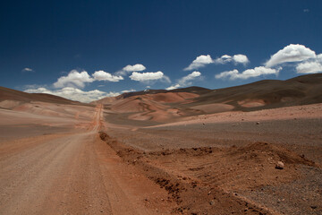 Fototapeta na wymiar The dirt road high in the Andes mountains. Traveling along the route across the arid desert and mountain range. The sand and death valley under a deep blue sky in La Rioja, Argentina.