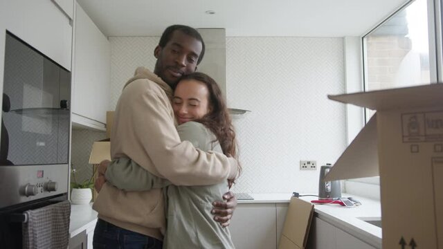 Close up of young mixed ethnicity couple standing in kitchen of new home hugging as they unpack removal boxes together - shot in slow motion