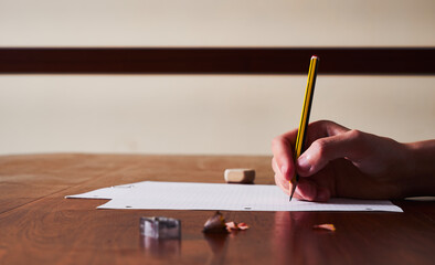 Women's hands writing with a pencil on soft checkered paper on a large wooden table