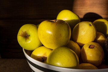 Manzanas amarillas y guayabas en un frutero blanco y negro, con luz de atardecer y madera de fondo