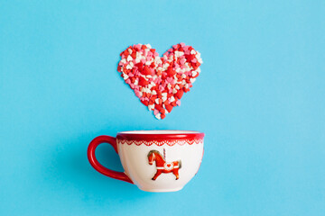 Valentine's Day background February 14th. Heart made of red, pink, white hearts confetti and cup on bright blue background. Valentines day creative concept. Flat lay, top view, copy space