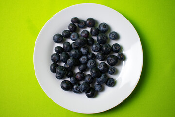 blueberries on a white plate with green background