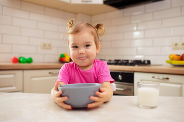 happy baby sitting at the table in the kitchen and eating with an appetite