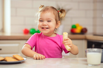 happy baby sitting at the table in the kitchen and eating with an appetite