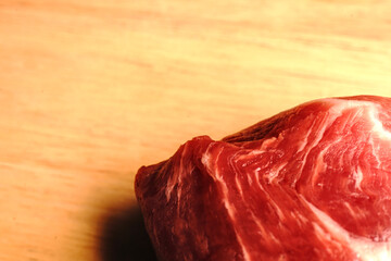 Red meat lies on a wooden board. Visible layers of fat and texture of meat. Pork