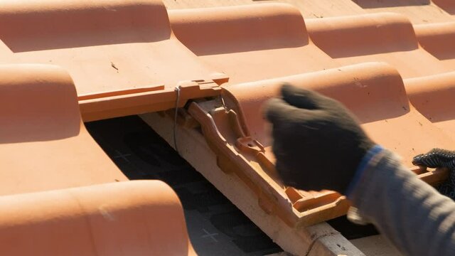 Closeup of worker hands installing yellow ceramic roofing tiles mounted on wooden boards covering residential building roof under construction.