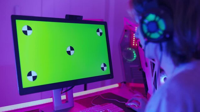 Gamer Playing and  Shooter Online Video Game on Powerful Personal Computer. Room and PC have Colorful Neon Led Lights.  Playing Online Video Game with a Mock Up Green Screen.