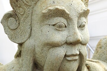 Closeup of ancient carved stone face with wide eyes and long mustache outside a temple in Southeast Asia
