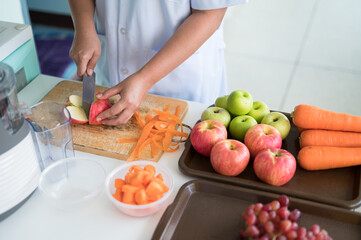 Woman  hand holding knife cutting red apple in kitchen.Woman juicing green and red apple fruits with carrots as part of her wellness food, detox smoothie.