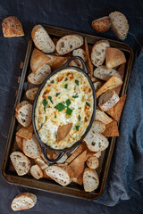 Top down view of a cookie sheet filled with various pieces of bread and pita triangles with artichoke dip in the middle.