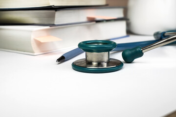 On a white background, a close-up of a stethoscope against a background of blurred books.