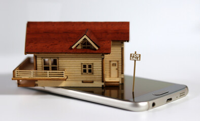 Miniature house with a sign written "For Sale" on the smartphone. The concept of non-face-to-face real estate brokerage.
