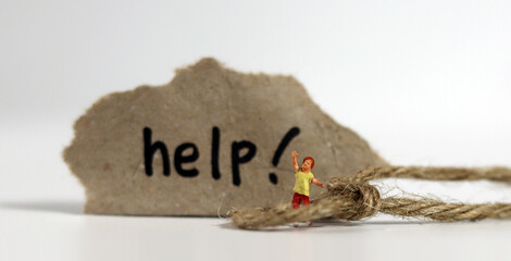 Miniature child surrounded by rope with paper written 'help'. The concept of warning against the increasing risk of domestic violence.
