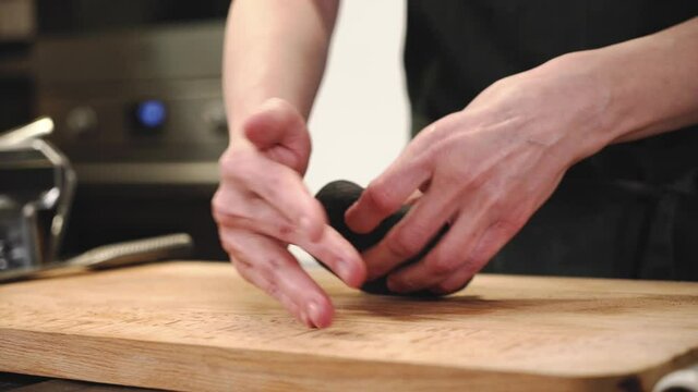 Black dough. Dough with cuttlefish ink. The chef is preparing the dough. Hands kneading the dough.