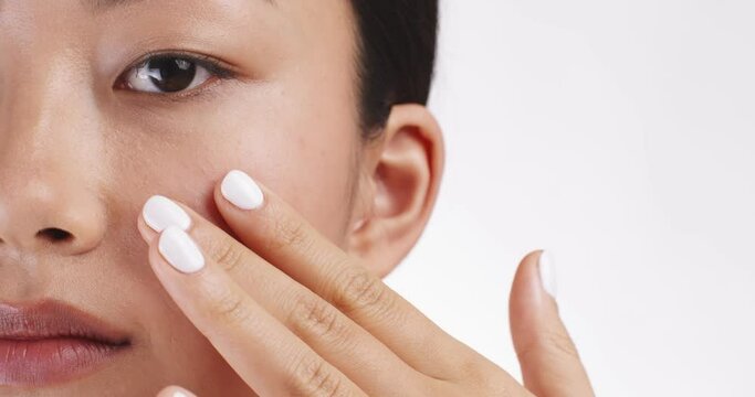 Half face portrait of young asian woman applying care cream on her cheek, white background, empty space