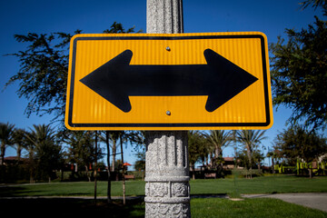 Yellow Road sign on a street pole with arrows pointed in opposite directions facing east and west...