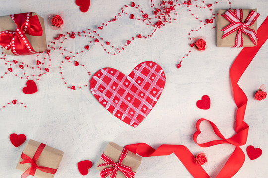 Heart from a red ribbon, gifts with a red ribbon and red hearts on a white stone background. Valentine's day background. Valentine's day concept. Flat lay.