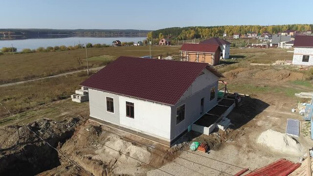Flying around of construction site with unfinished modern energy efficient house of foam blocks panels with roof with metal tile sheets. House in village near the lake. Sunny day
