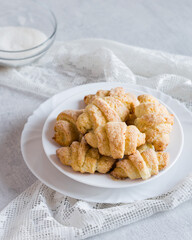 Homemade cottage cheese cookies bagels rogaliki with sugar on white plate on grey background, selective focus