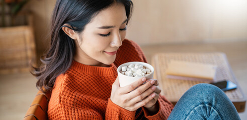 Closeup young beautiful asian woman in sweater hands holding a cup of coffee morning winter time...