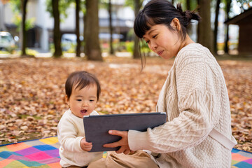 秋の公園でママとタブレットPCで遊ぶ赤ちゃん
