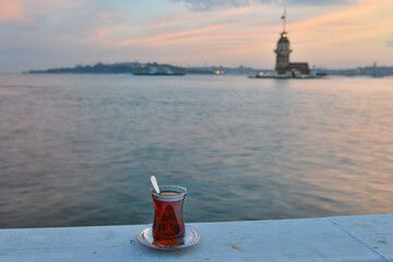 A glass of traditional  Turkish tea and historical Maiden's Tower or Kiz Kulesi during sunset  - Istanbul, Turkey.
