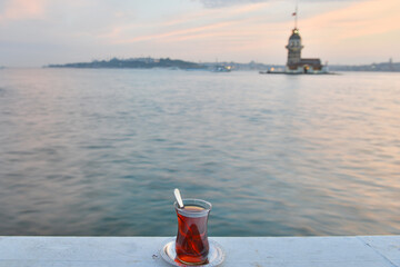 A glass of traditional  Turkish tea and historical Maiden's Tower or Kiz Kulesi during sunset  - Istanbul, Turkey.
