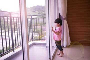 an asian girl is looking out the window in the living room alone