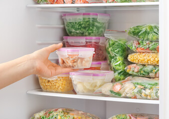 Woman putting container with frozen vegetables into refrigerator