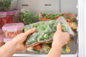 Woman putting plastic bag with frozen vegetables into refrigerator