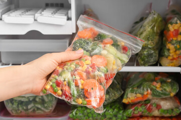 Woman putting plastic bag with frozen vegetables into refrigerator