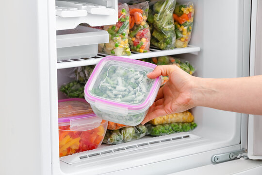 Woman Putting Container With Frozen Vegetables Into Refrigerator